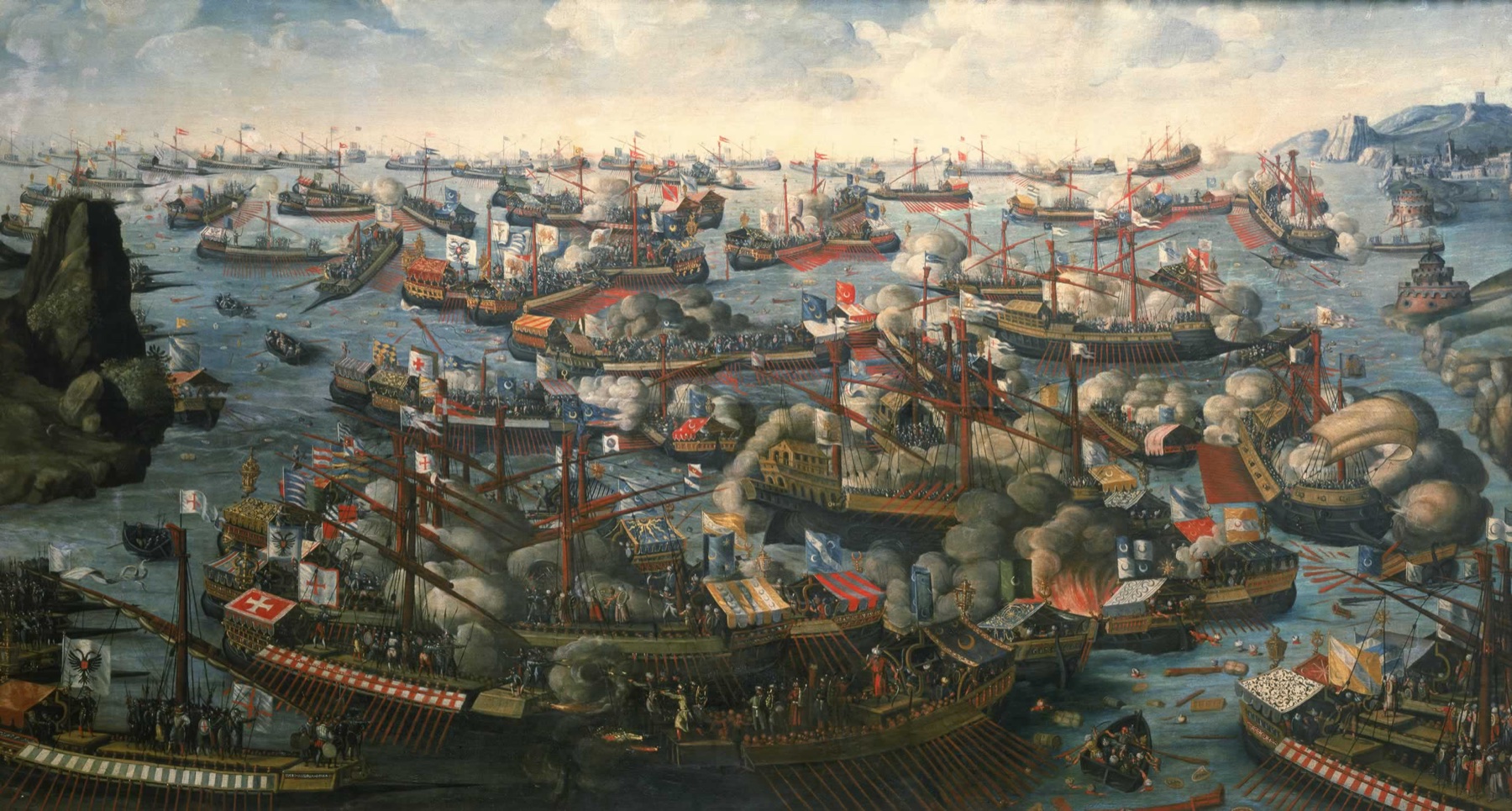 An oil painting of a sea crowded from edge to edge with war galleys under banners and gunsmoke, oars out, soldiers packed along the decks, a rocky headland at the left and a fortified town on the far shore at the right