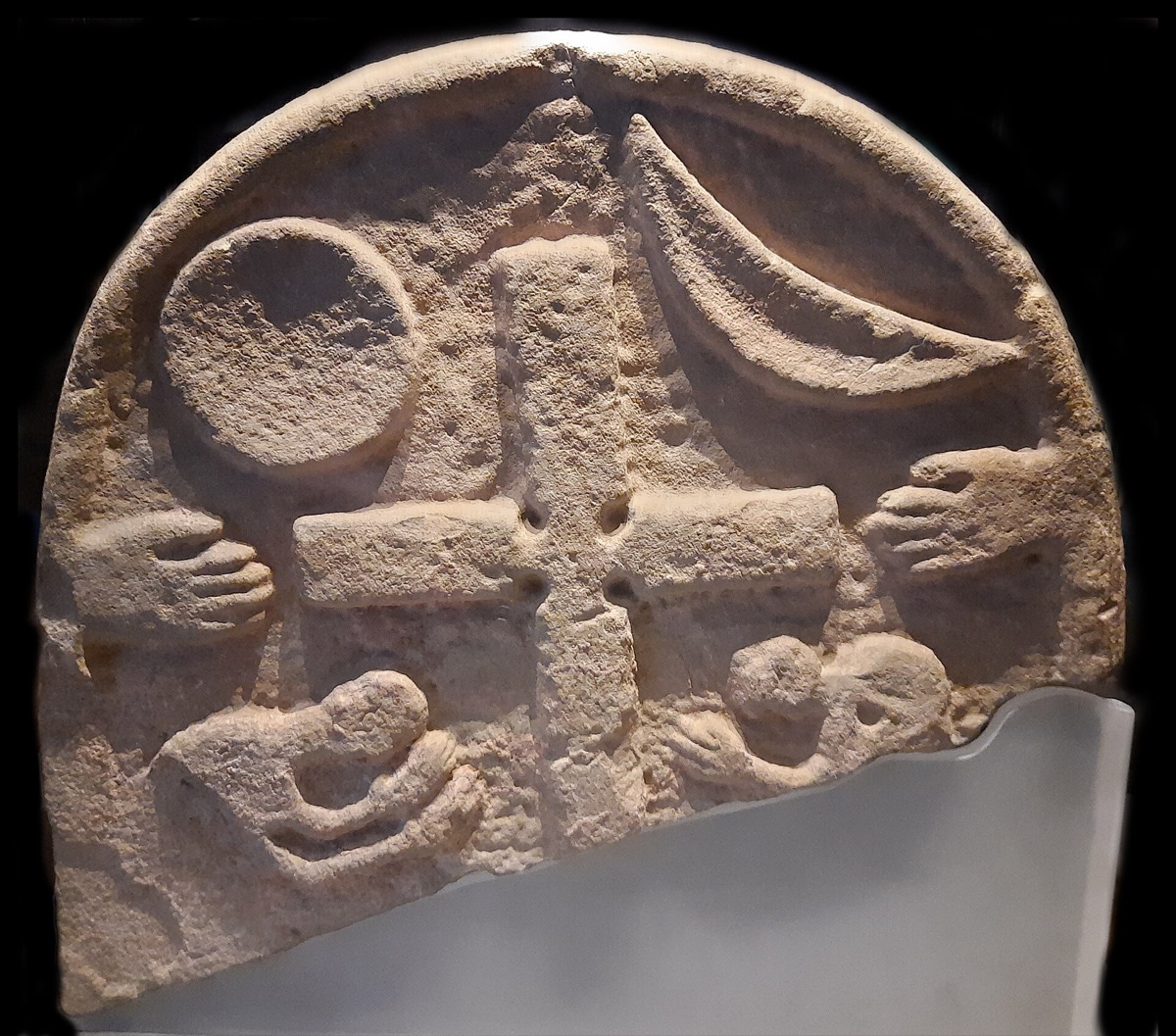 The other face of the same stone: a cross flanked by sun and moon, with raised praying hands and kneeling figures below