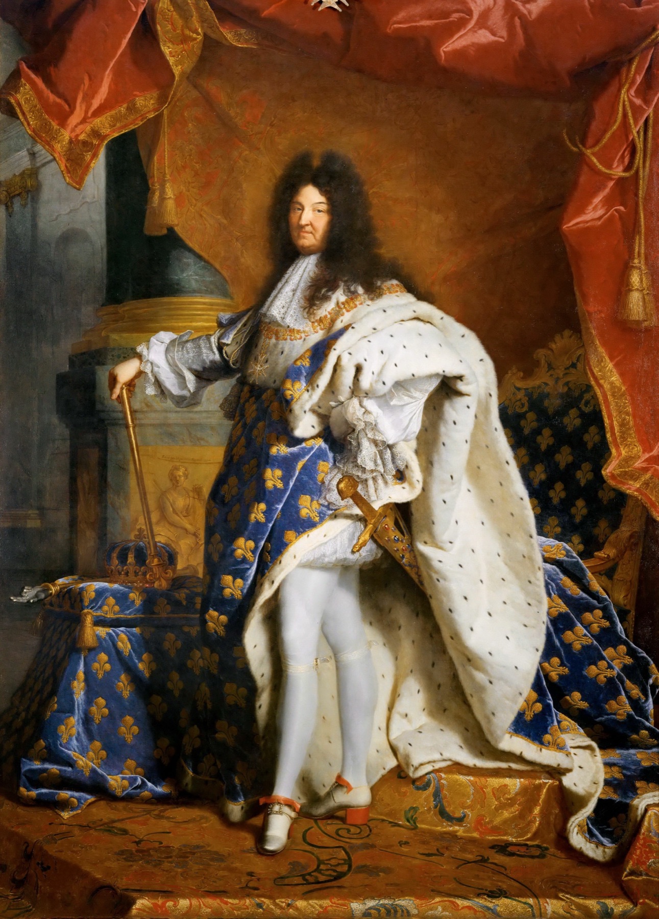 Full-length portrait of Louis XIV in ermine-lined blue and gold coronation robes, hand on a cane, crown resting on a cushion beside him