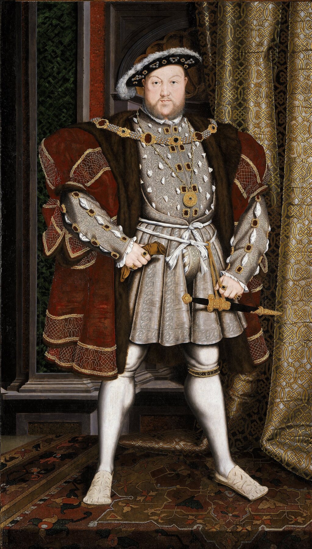 A full-length painted portrait of Henry VIII: feet planted wide, padded shoulders filling the frame, jewelled collar and dagger, standing on a patterned carpet before a curtain