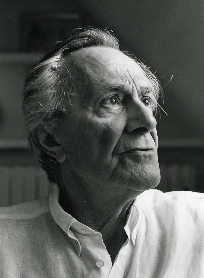 A black and white photograph of an elderly man with untidy white hair, in a white open-necked shirt, looking up and to the side