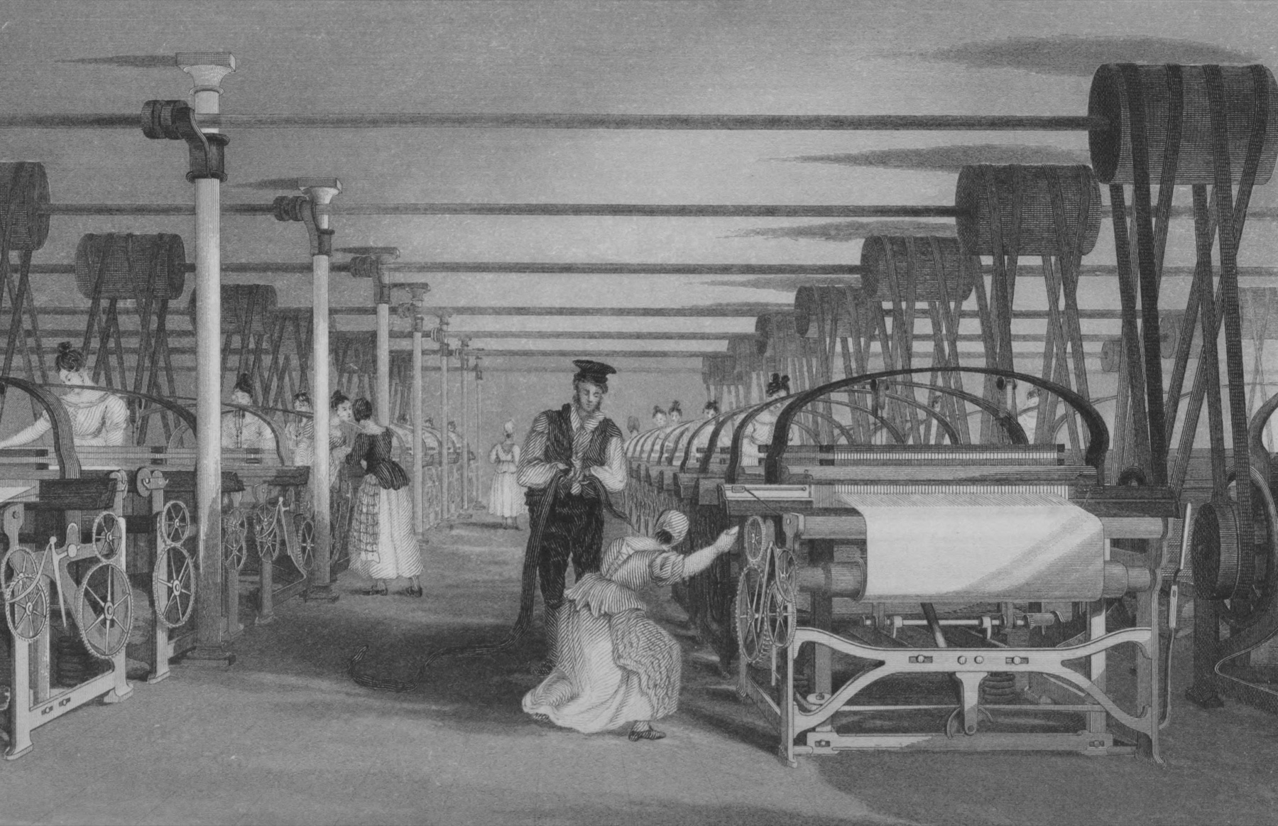 An engraving of a long factory hall with two rows of power looms receding into the distance, driven by belts from shafting that crosses the ceiling, tended almost entirely by women and girls in long dresses