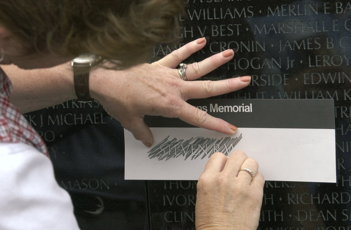 A visitor presses paper against the polished black granite of the Vietnam Veterans Memorial and takes a pencil rubbing of one engraved name