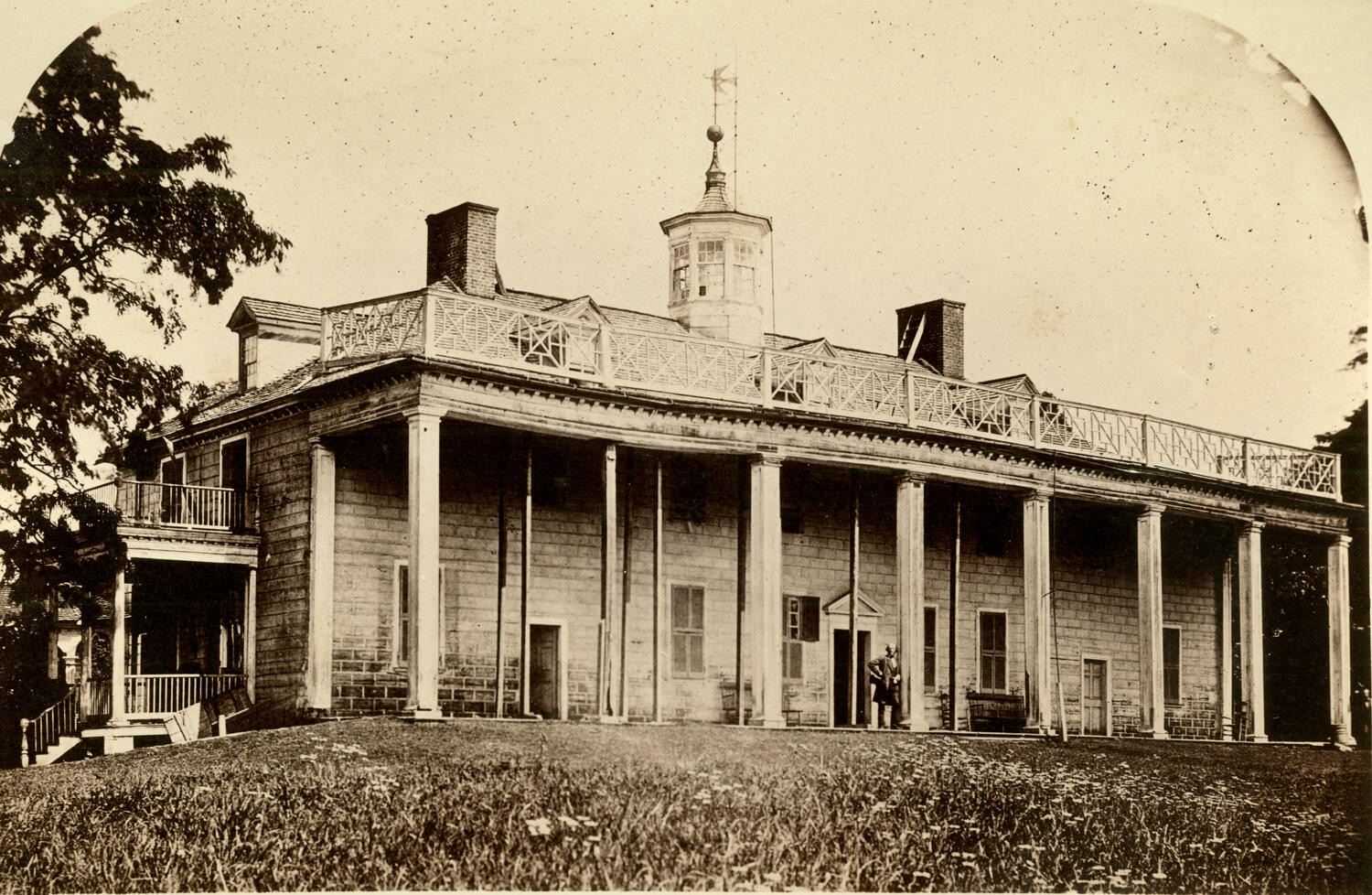 A photograph of a large colonnaded plantation house in visible disrepair, its piazza roof propped up by rough timbers and ship's masts where the pillars have collapsed
