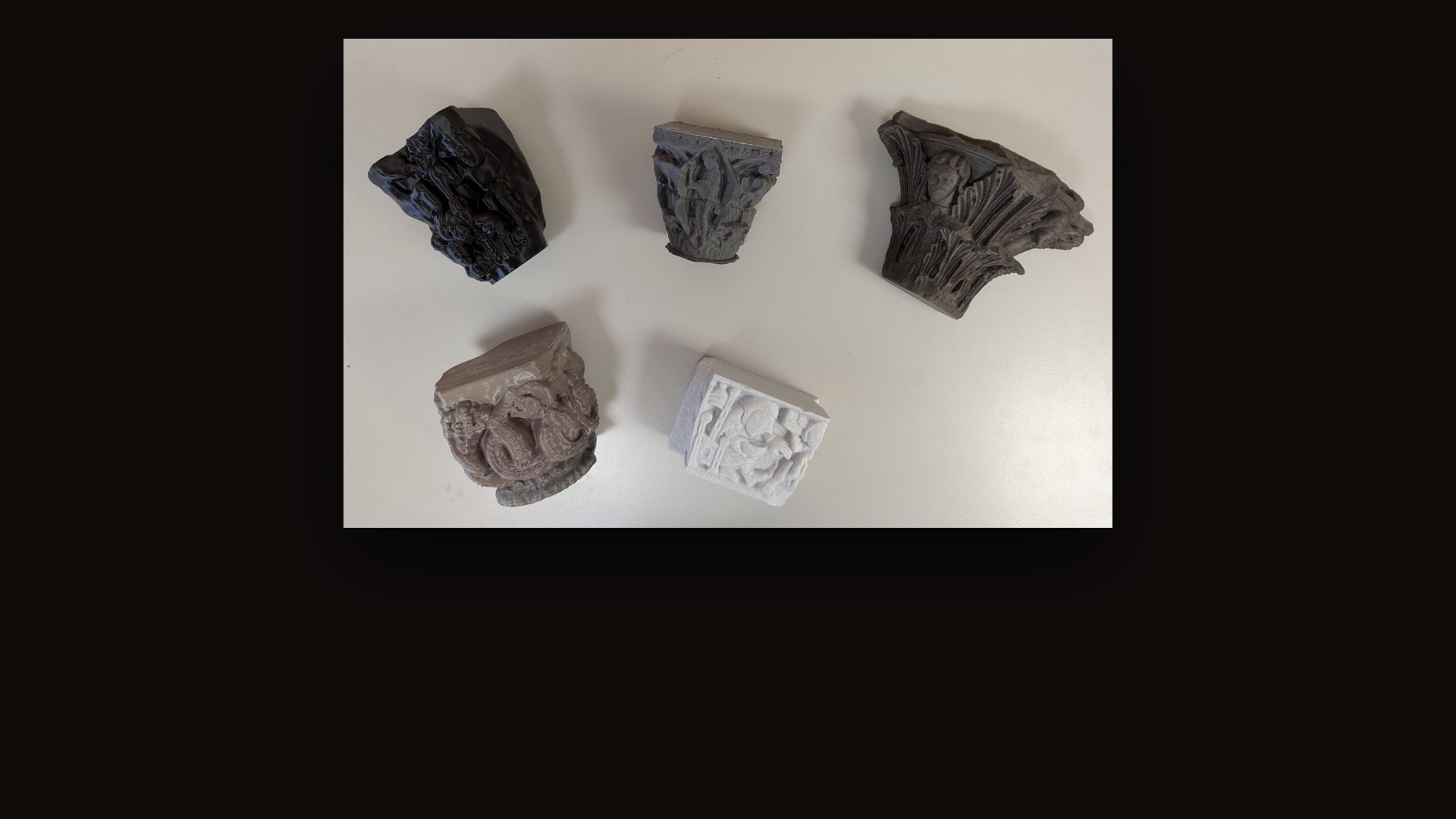 Five 3D-printed medieval capitals in different filaments, laid out on a white table