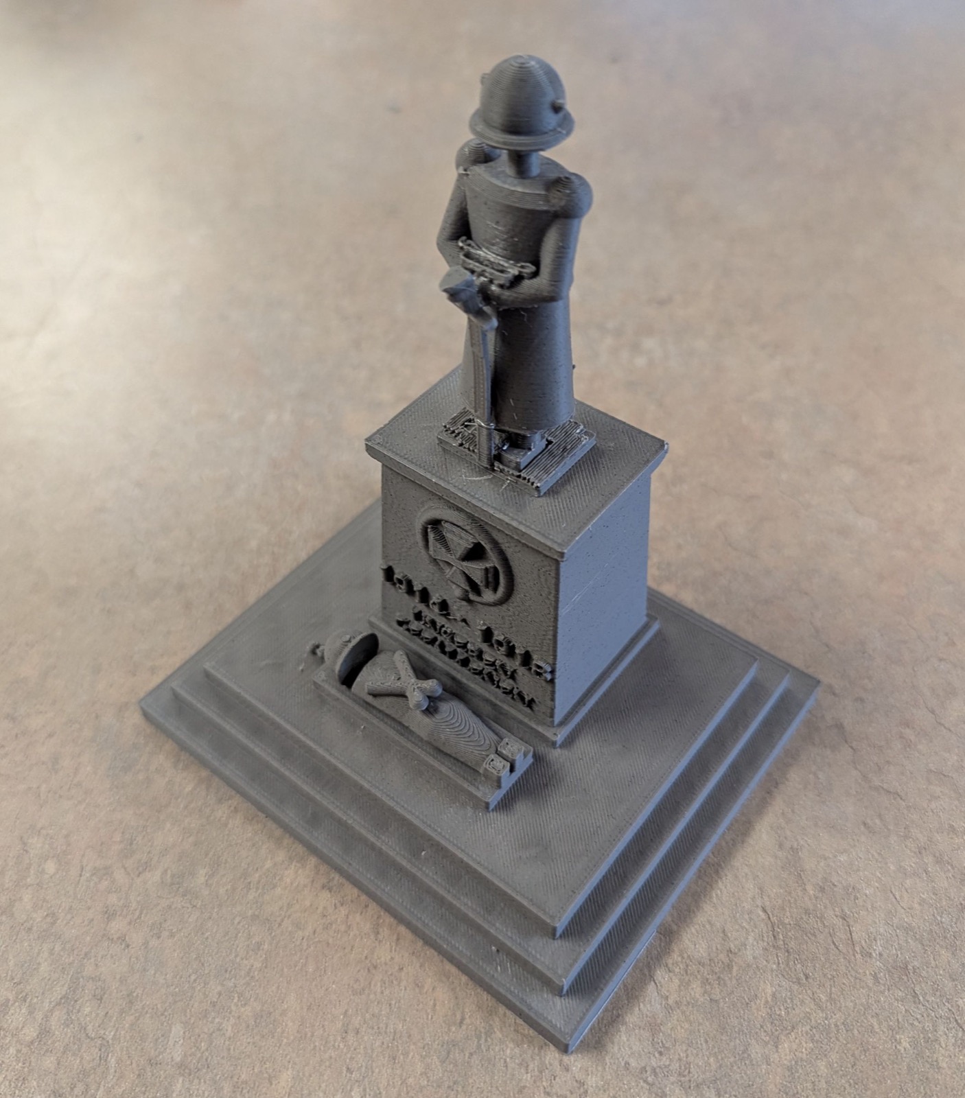 A grey 3D print of an imaginary 1920s German war memorial: a stepped plinth carrying an Iron Cross in a wreath and an inscription, a helmeted sentry resting both hands on a sword above, and a recumbent soldier lying at its foot